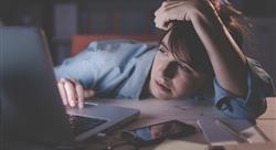 young woman with head resting on her desk while on her computer with a bored look on her face