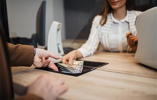Businesswoman is working in exchange office. She is giving cash money to male customer.