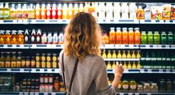 back view of young woman looking at bottle of juice in grocery store