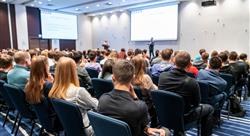 People sitting in a large conference room listening to a presenter in the front of the room