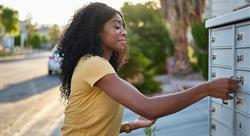 woman wearing yellow shirt and gold watch checking her mailbox near the curb