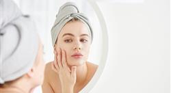 Portrait of young girl with towel on head in white bathroom looks and touches her face in the mirror